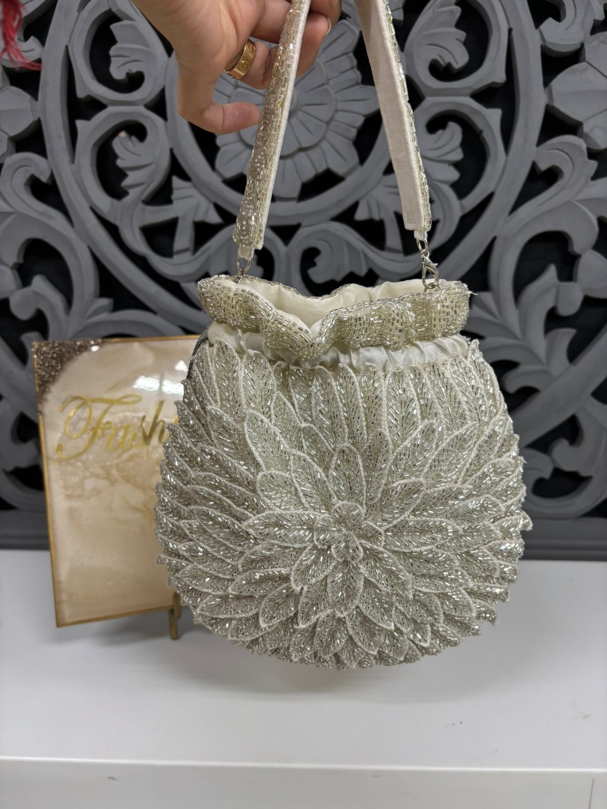Silver glittery handbag with decorative handle against a decorative white background
