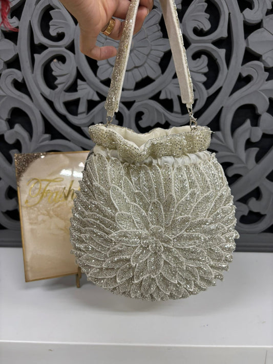 Silver glittery handbag with decorative handle against a decorative white background