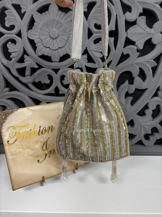 Drawstring bag with gold and silver stripes held by a hand against a decorative wall.