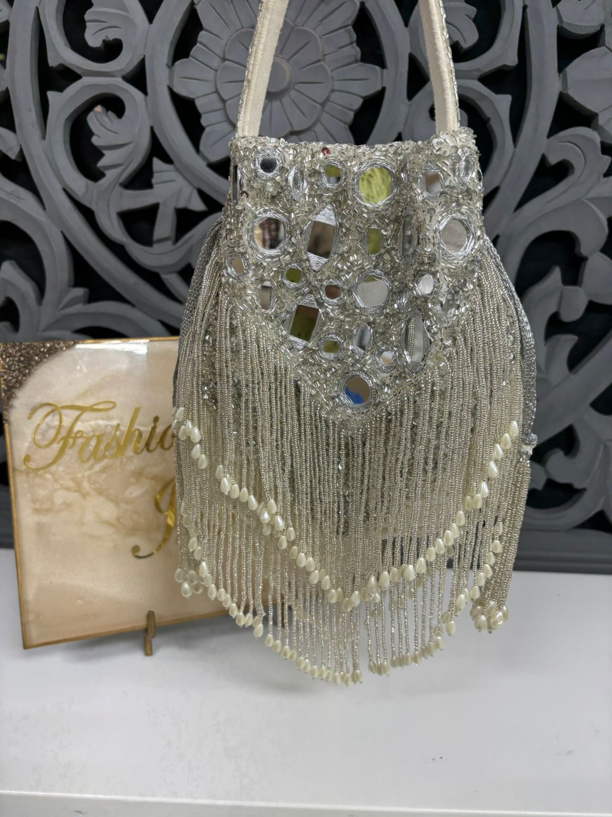 Decorative handbag with beads and mirror-like stones on a textured surface.