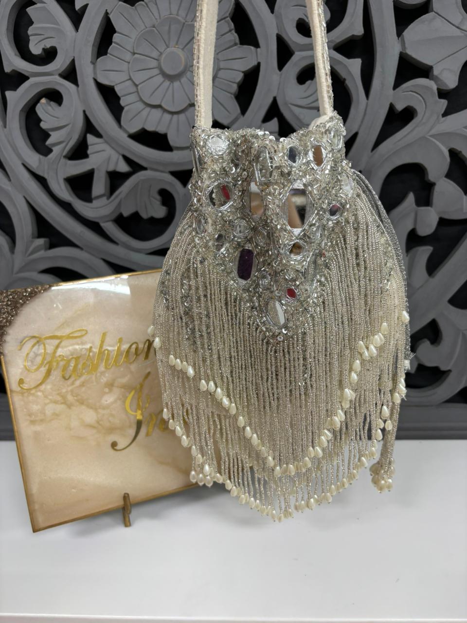 Decorative handbag with intricate design and tassels on a white surface with a decorative background.
