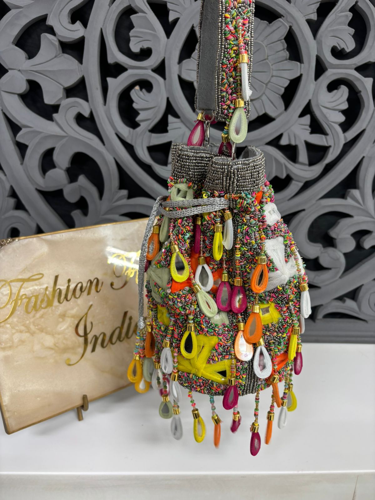 Colorful beaded handbag with decorative elements on a white surface with a decorative wall in the background.