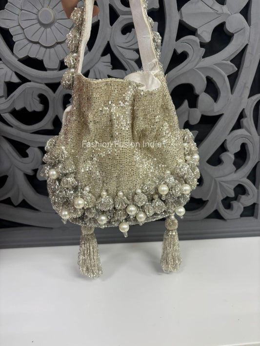 Decorative handbag with pearls and tassels on a white surface with a decorative gray background.