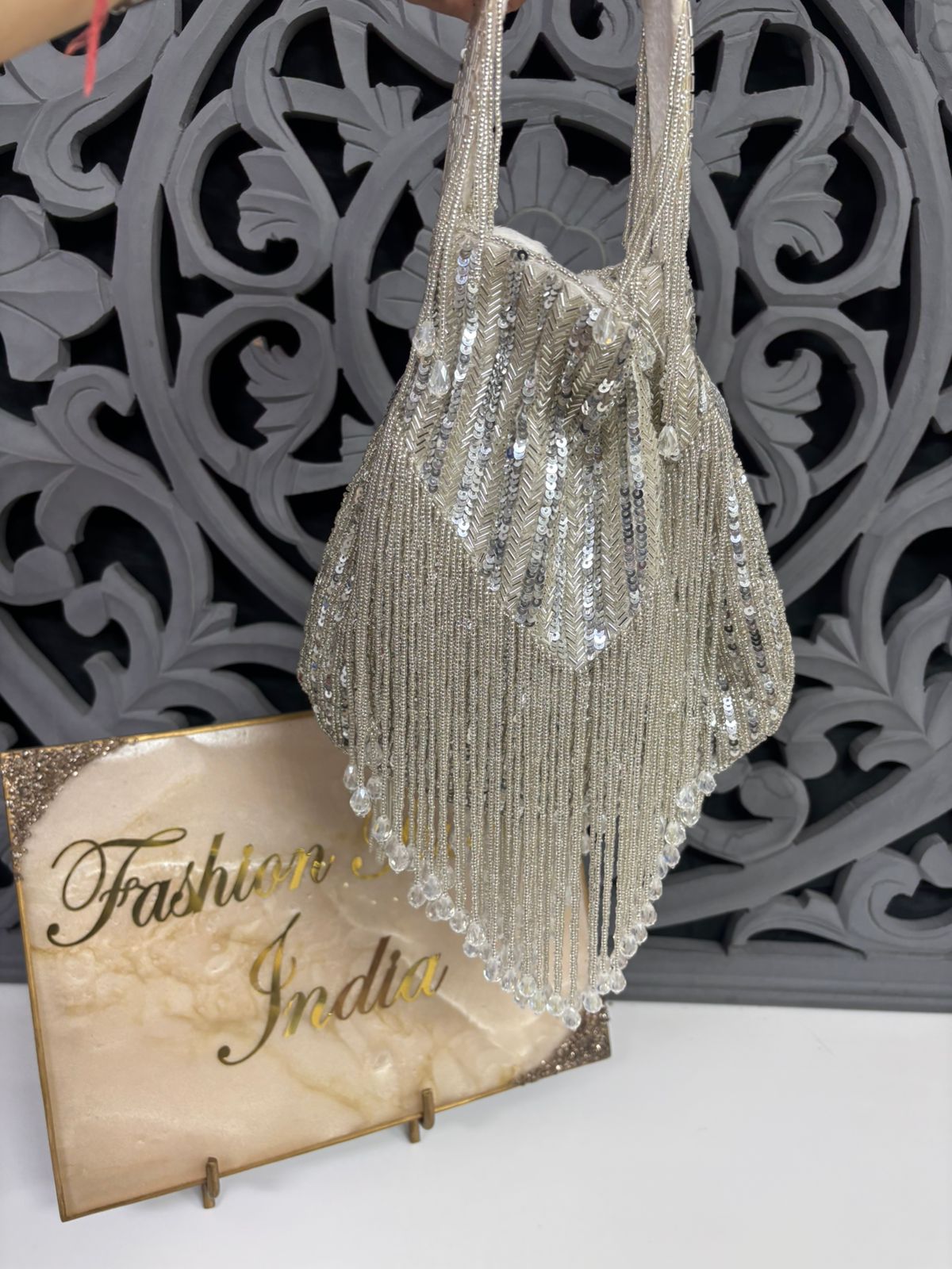 Silver sequin handbag with decorative stand and 'Fashion India' sign in the background
