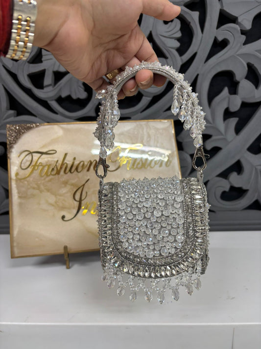 Silver embellished handbag held by a hand with a decorative background