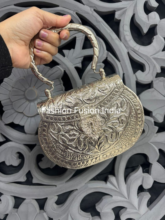 Silver handbag with intricate designs held by a hand against a decorative background, branded 'Fashion Fusion India'.