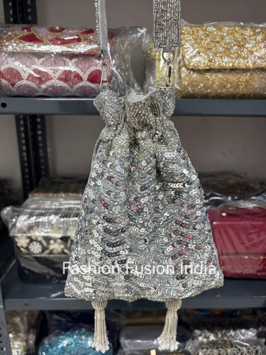 Silver sequin handbag with a decorative strap on a blurred background of other bags.