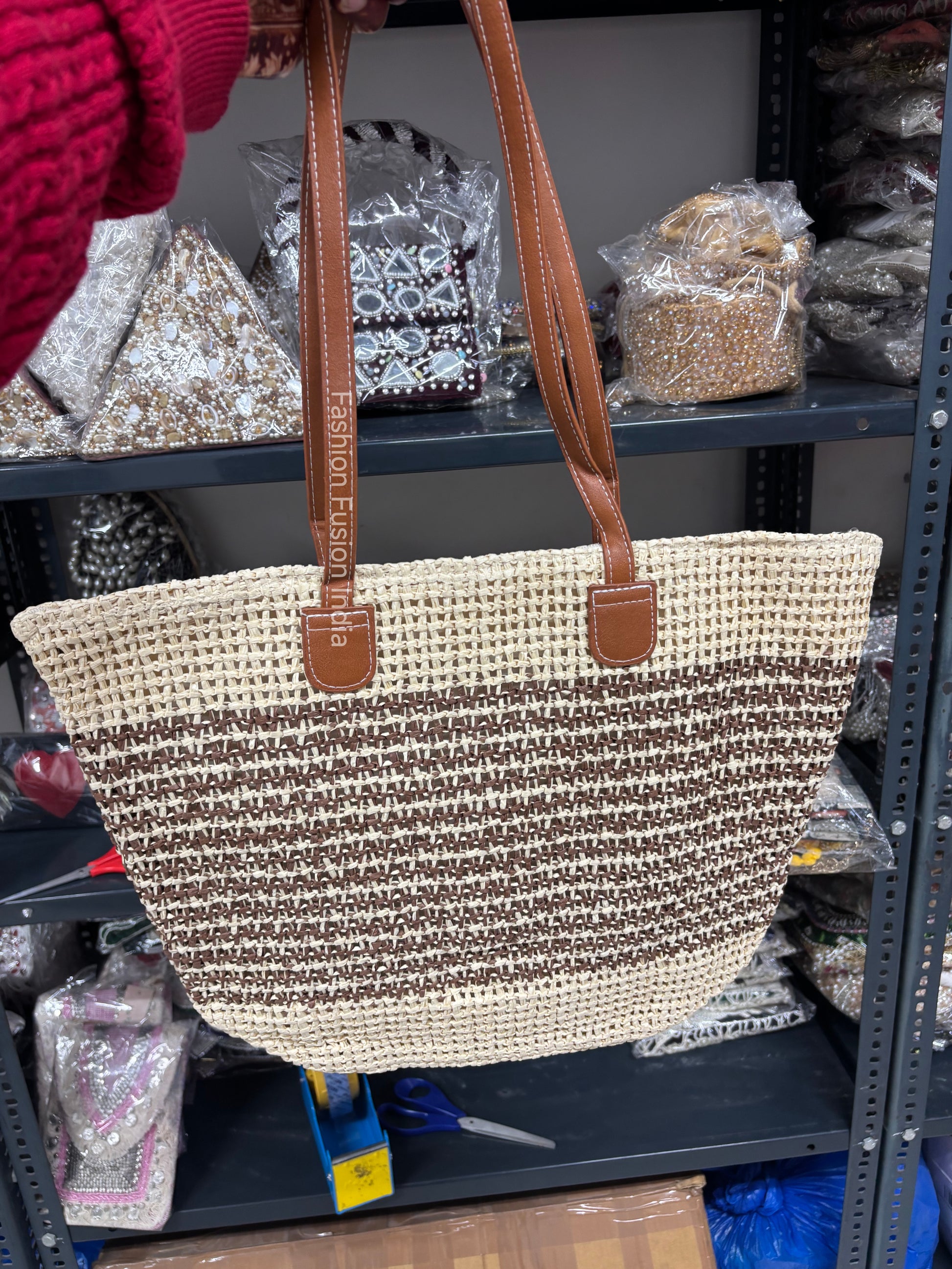 Woven handbag with brown straps held in front of a store shelf.