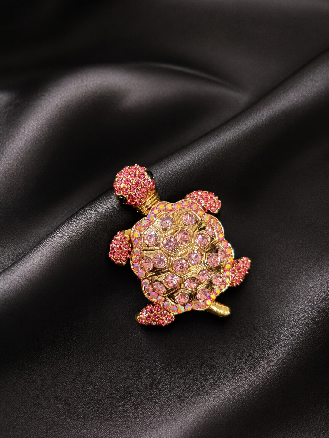 Decorative turtle brooch with pink gemstones on a black satin background