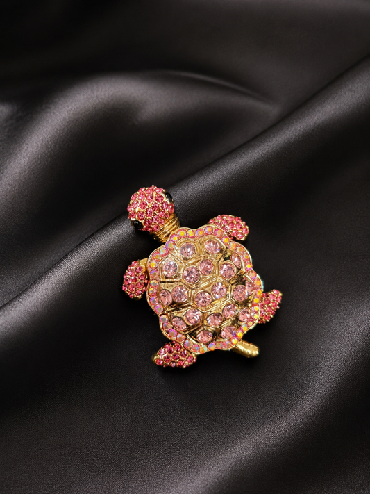 Decorative turtle brooch with pink gemstones on a black satin background