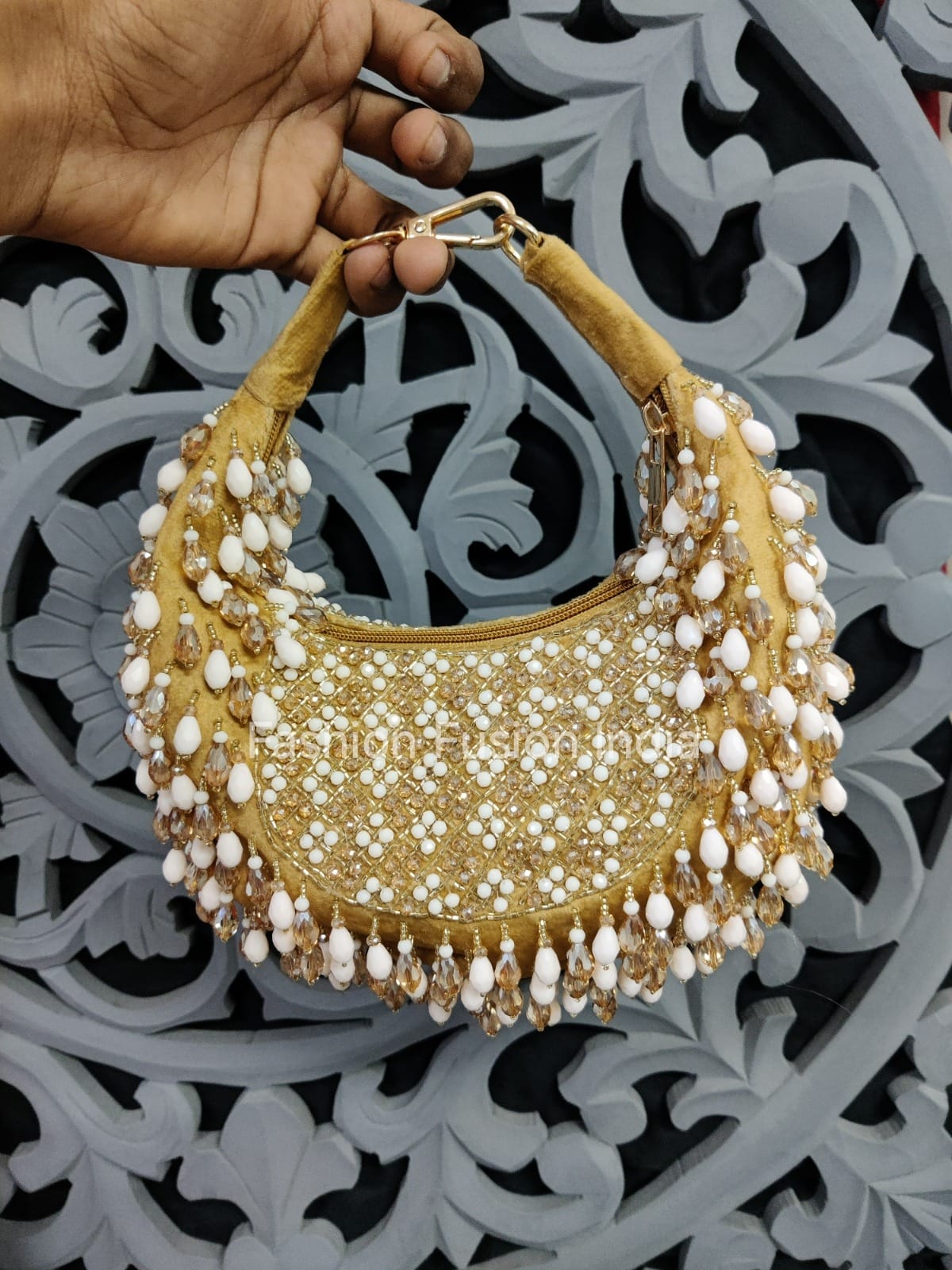 Gold handbag with pearl embellishments held by a hand against a decorative background