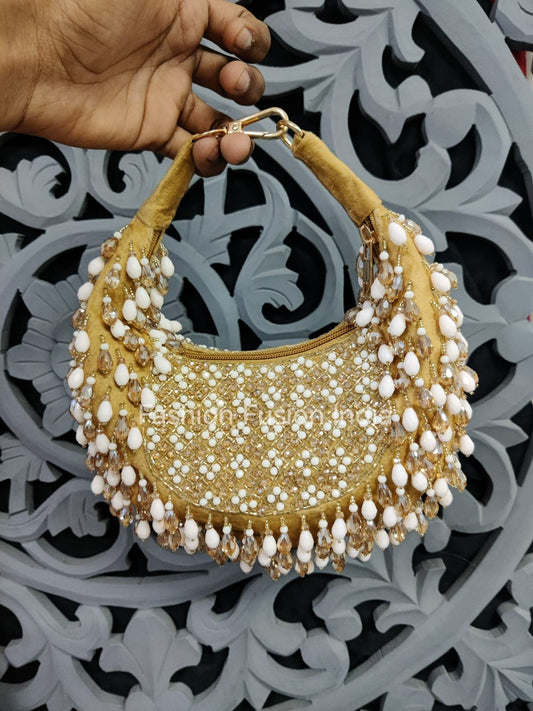Gold handbag with pearl embellishments held by a hand against a decorative background