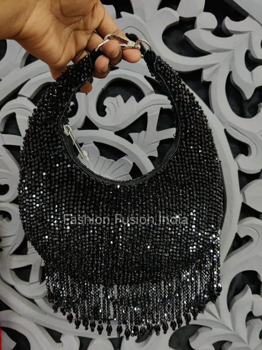 Black beaded handbag held by a hand against a decorative black and white background.