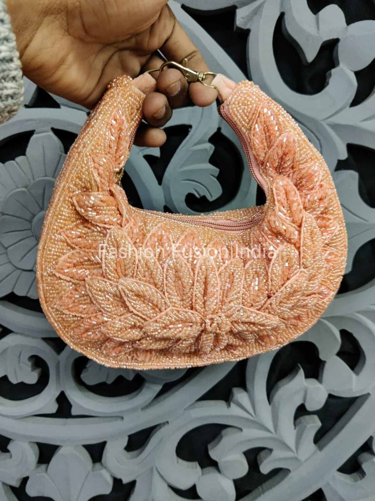 Hand holding a textured orange handbag against an intricate metal background
