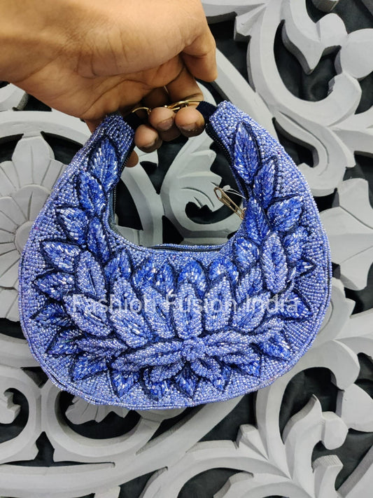 Blue beaded handbag held by a hand against an ornate white and black background