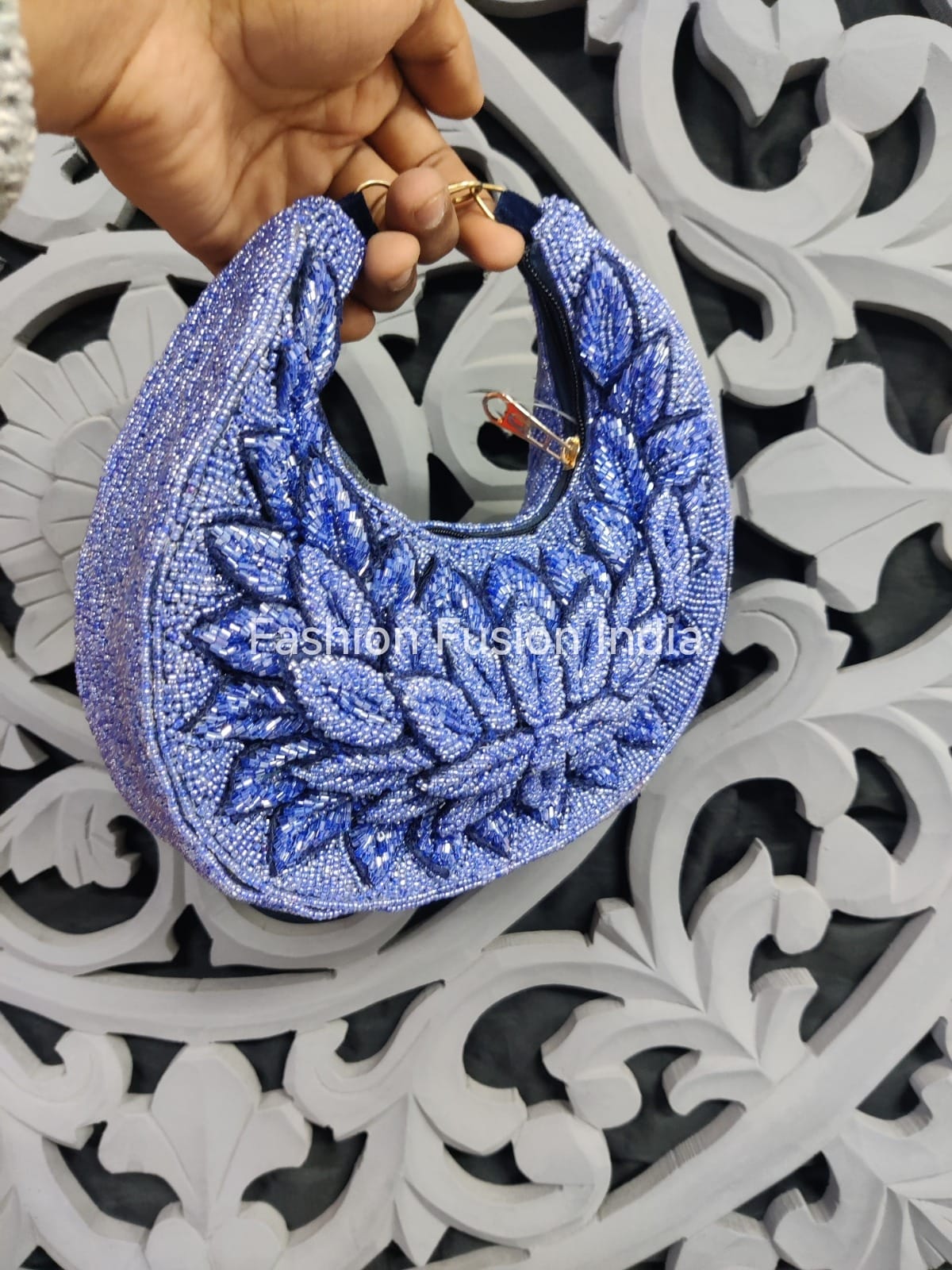 Blue beaded clutch held by a hand on an ornate white and black background