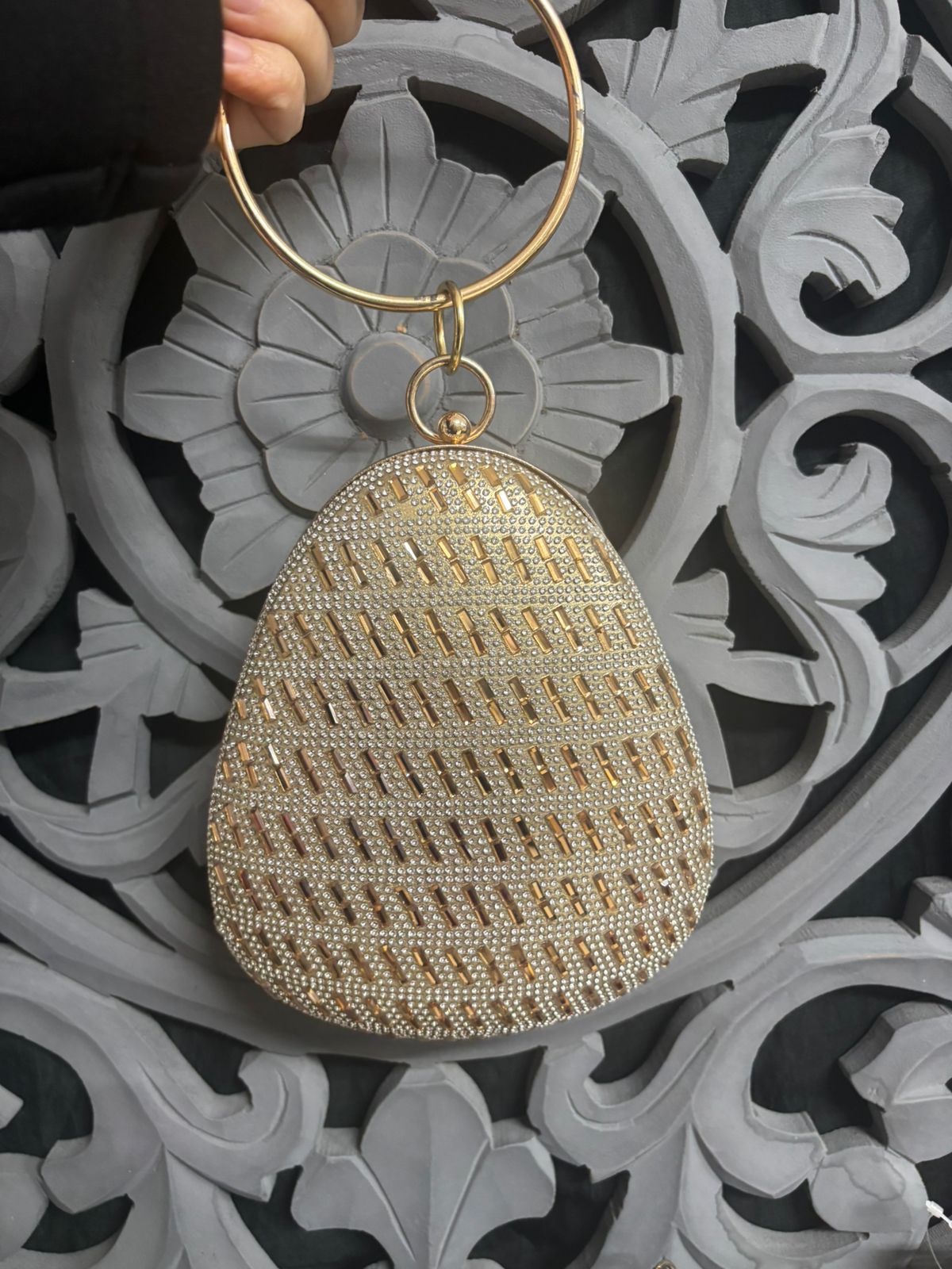 Gold beaded clutch held by a hand against an ornate gray and black background