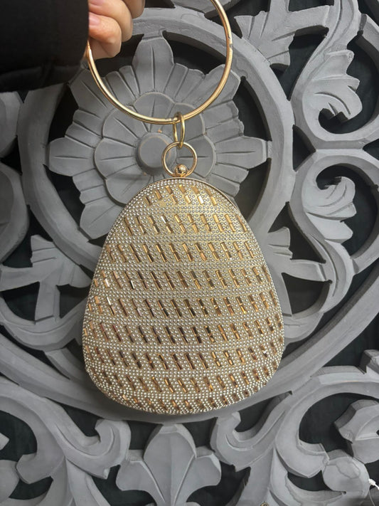 Gold beaded clutch held by a hand against an ornate gray and black background