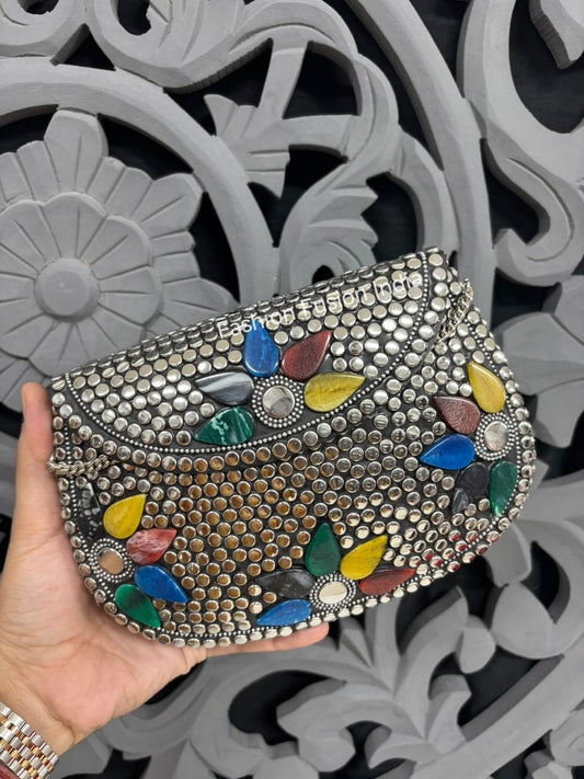 Handheld decorative clutch with colorful stones against a gray floral-patterned background