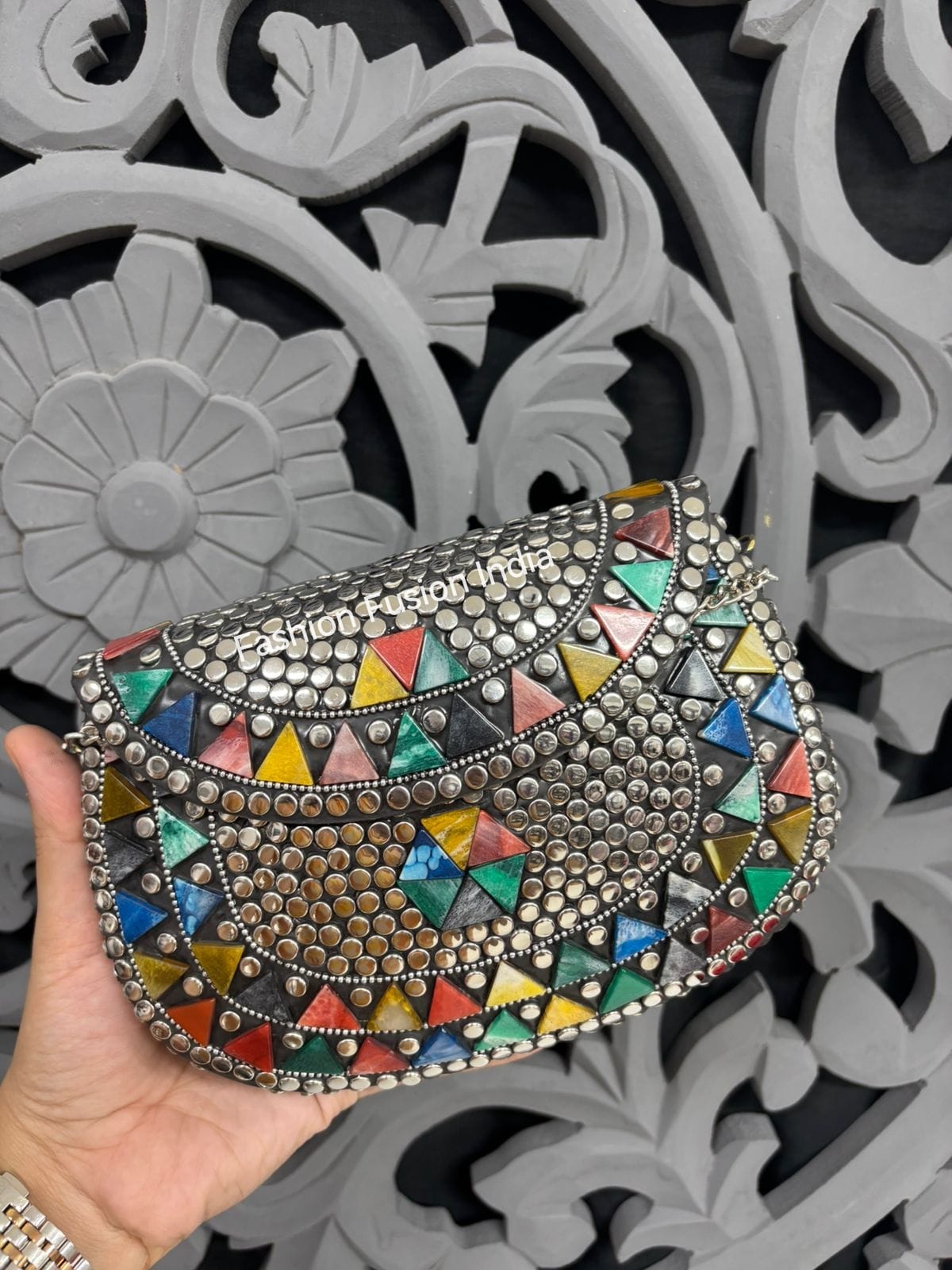 Decorative clutch with colorful triangle patterns held against a decorative gray background