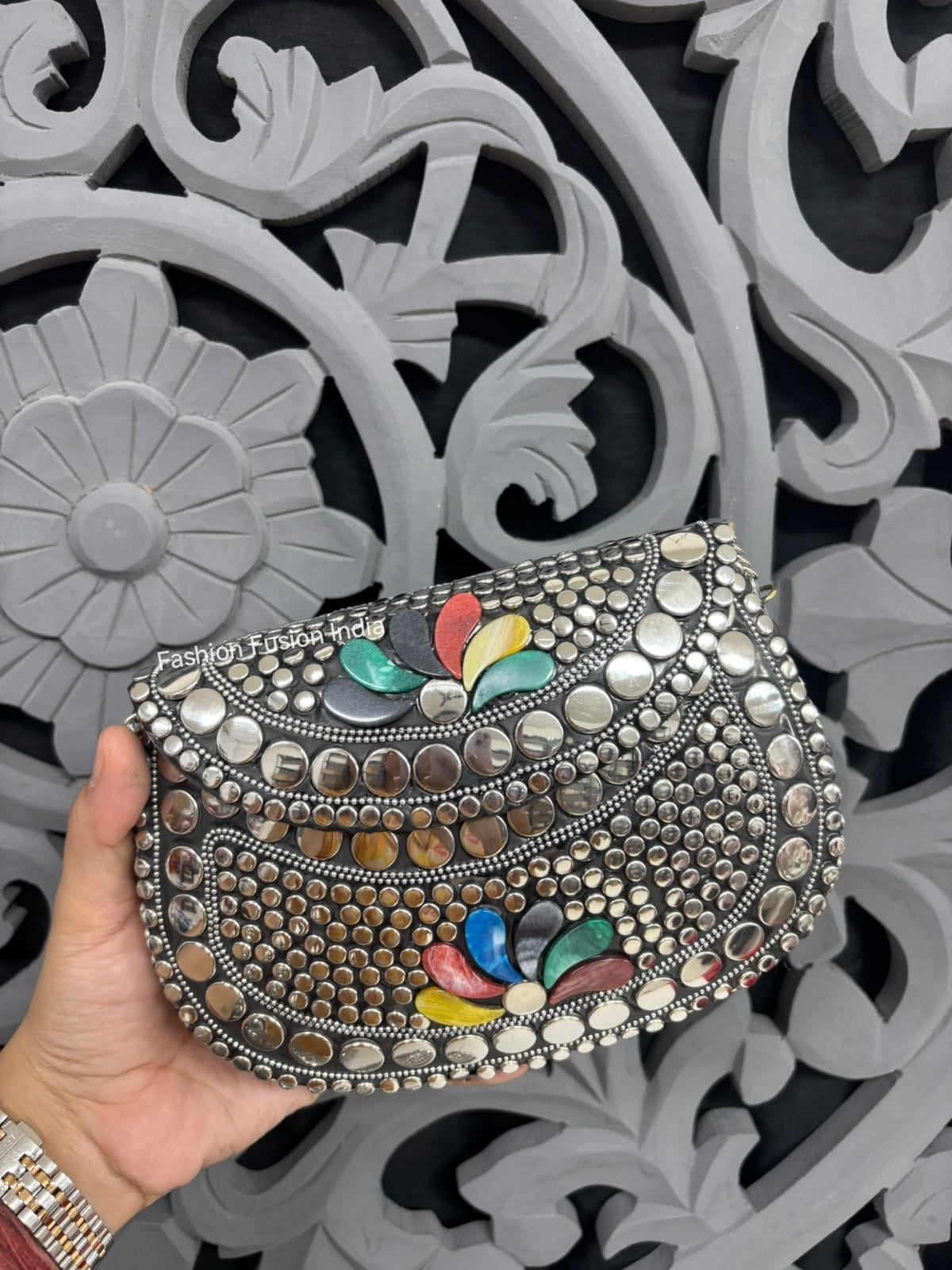 Decorative handbag with colorful accents held against an ornate gray background