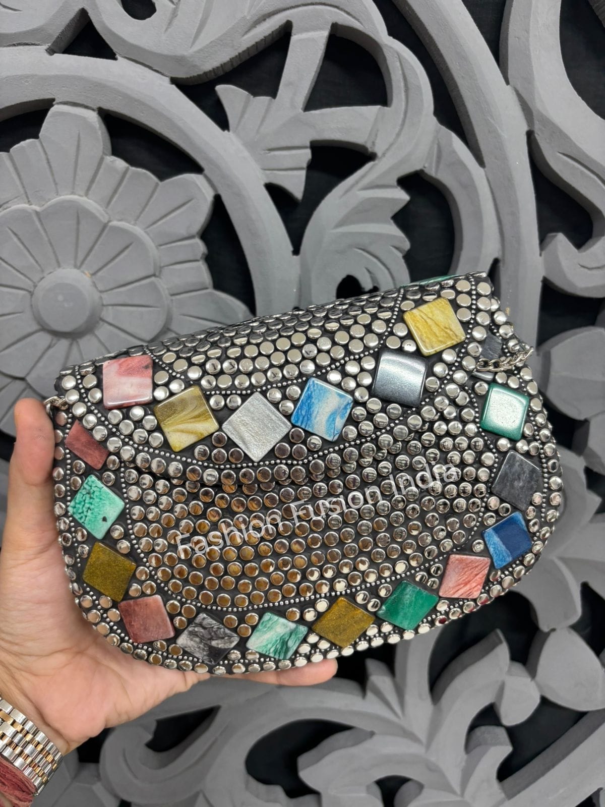 Handheld clutch with colorful gemstones against a decorative gray background
