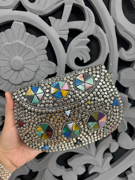 Decorative clutch with colorful gemstones held by a hand against an ornate gray background