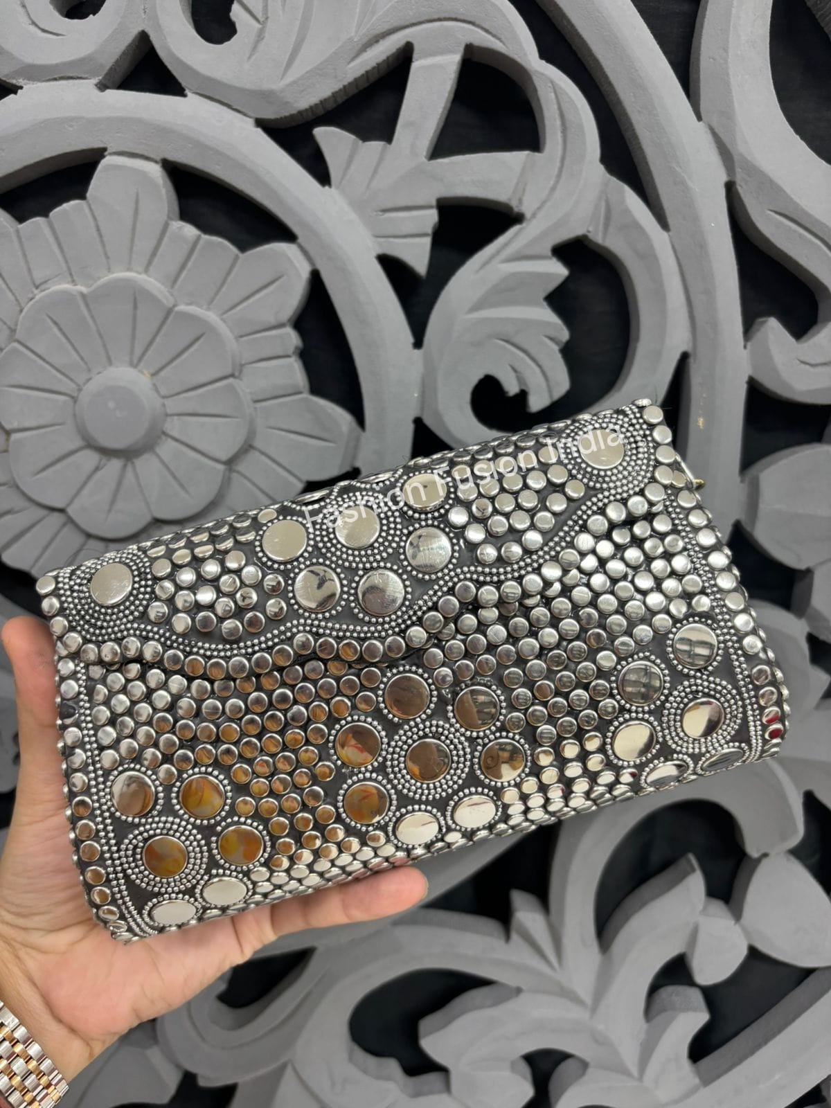 Decorative clutch with metallic embellishments held against a decorative gray background