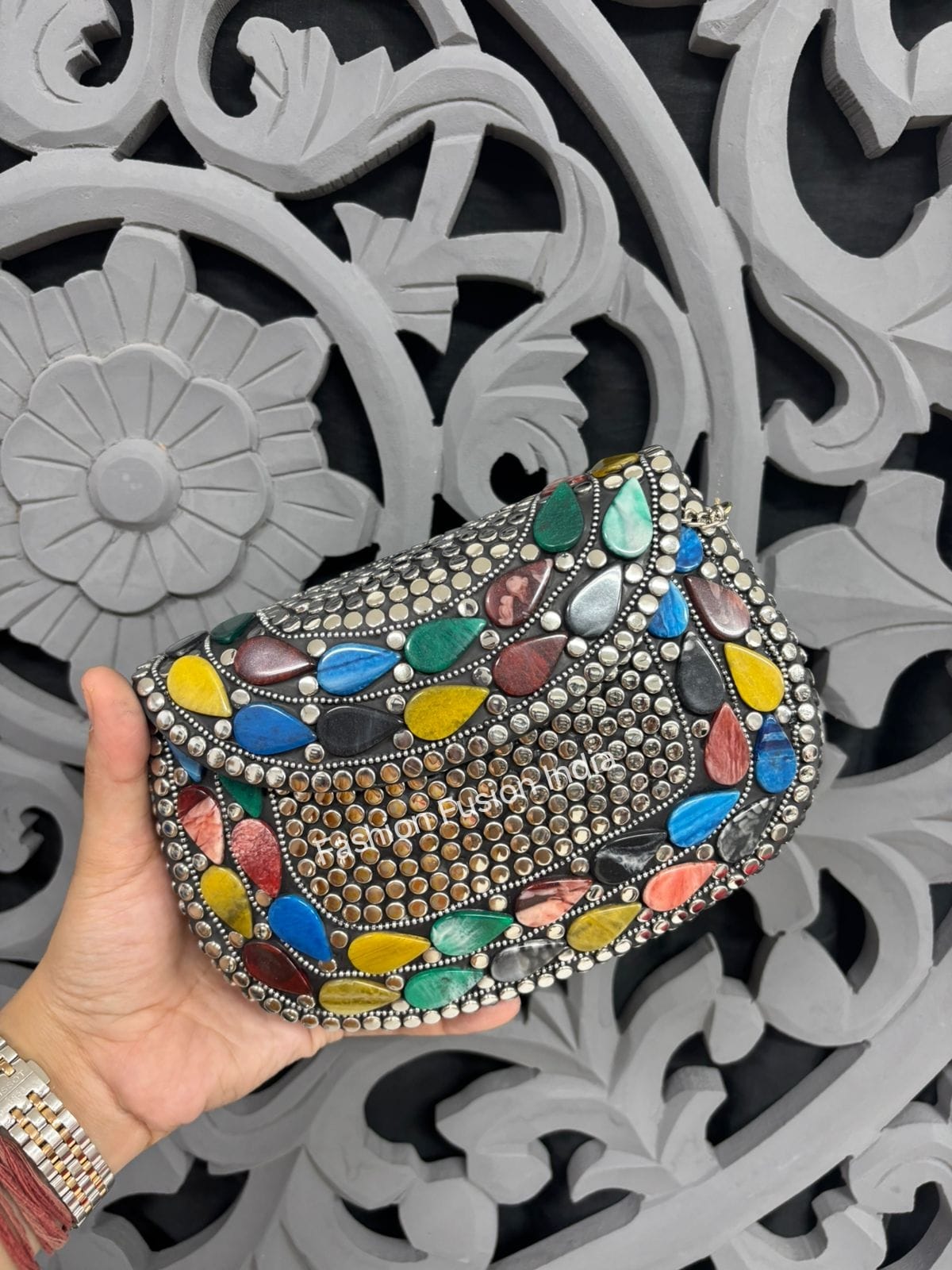 Colorful embellished clutch held by a hand against an ornate black and white background