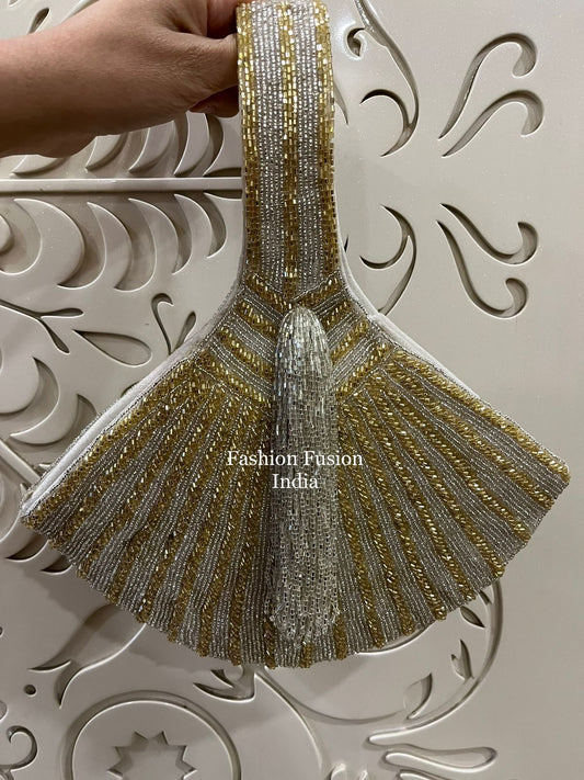 Hand holding a gold and silver beaded embroidered applique with an elegant fan-shaped design against a cream decorative background.