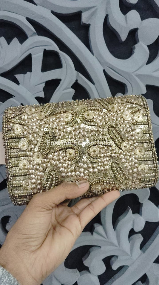 Gold beaded clutch held by a hand against a decorative black and white background