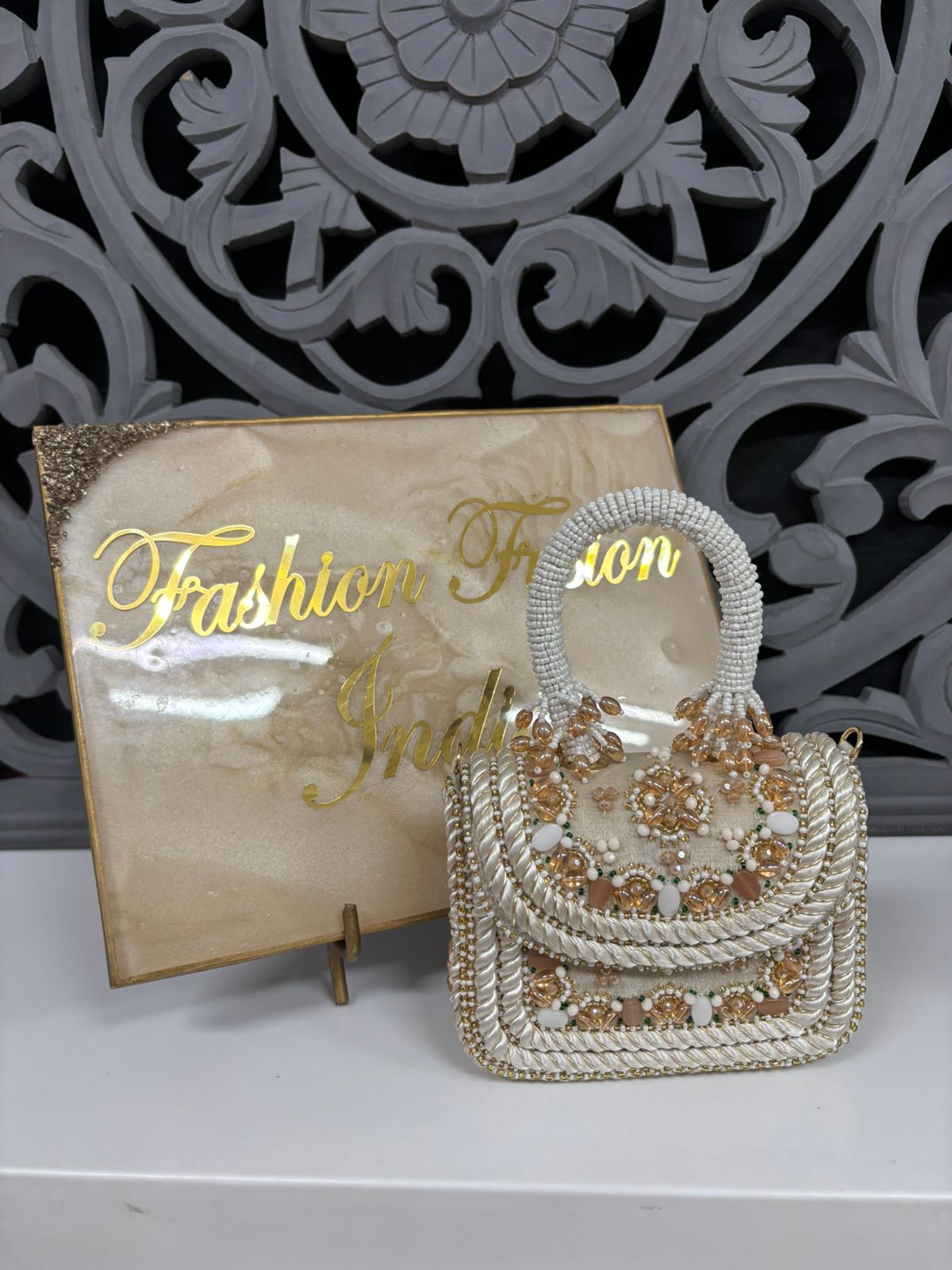 Decorative handbag with floral patterns on a stand with 'Fashion Fusion India' sign in the background.