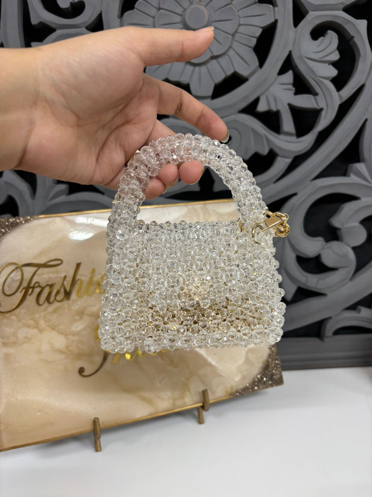 Hand holding a crystal-handled handbag with a decorative background