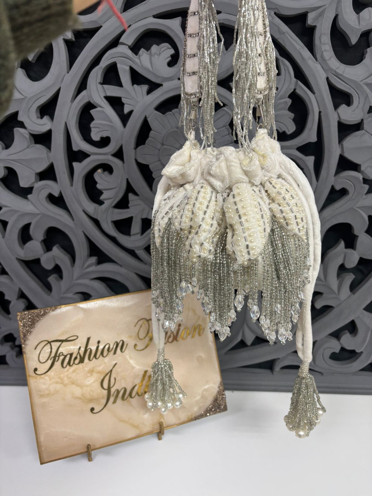 Decorative handbag with beaded details and tassels on a white surface with 'Fashion Designer India' sign.