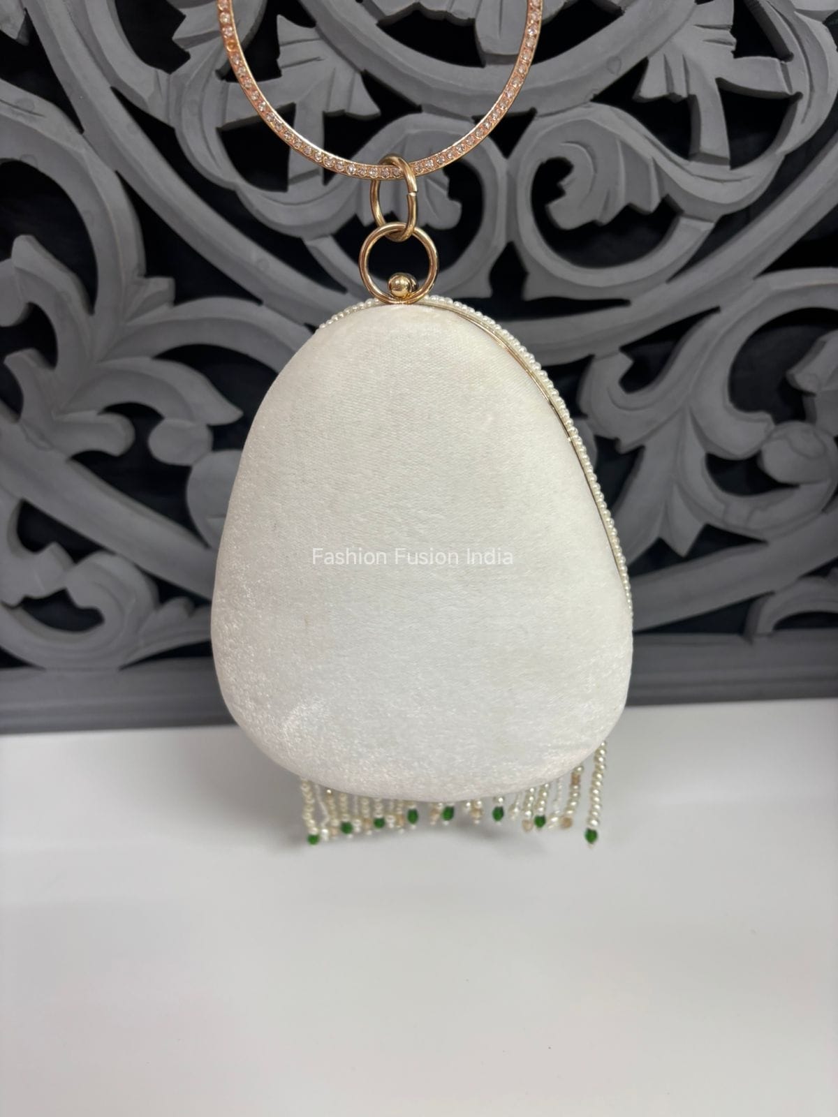 White clutch with gold chain and green beads against a decorative gray background
