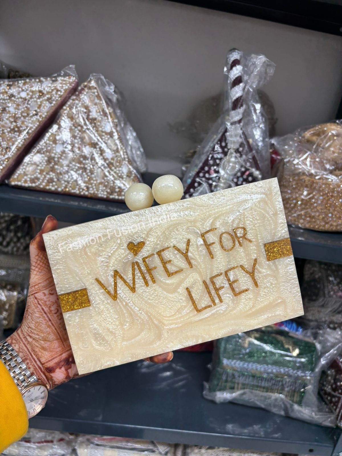 Card with 'WIFEY FOR LIFELY' text held by a hand in front of wrapped gifts.