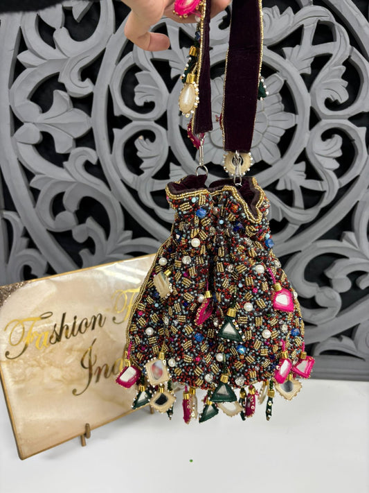 Decorative handbag with beads and gemstones held by a hand, with 'Fashion India' magazine in the background.