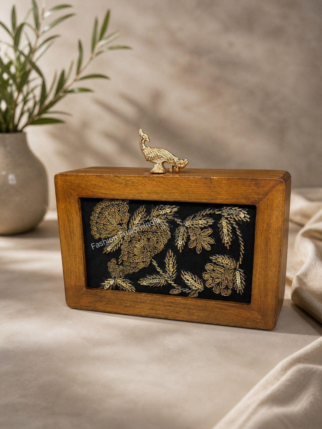 Wooden clutch with gold floral embroidery and peacock clasp in a soft luxury setting.