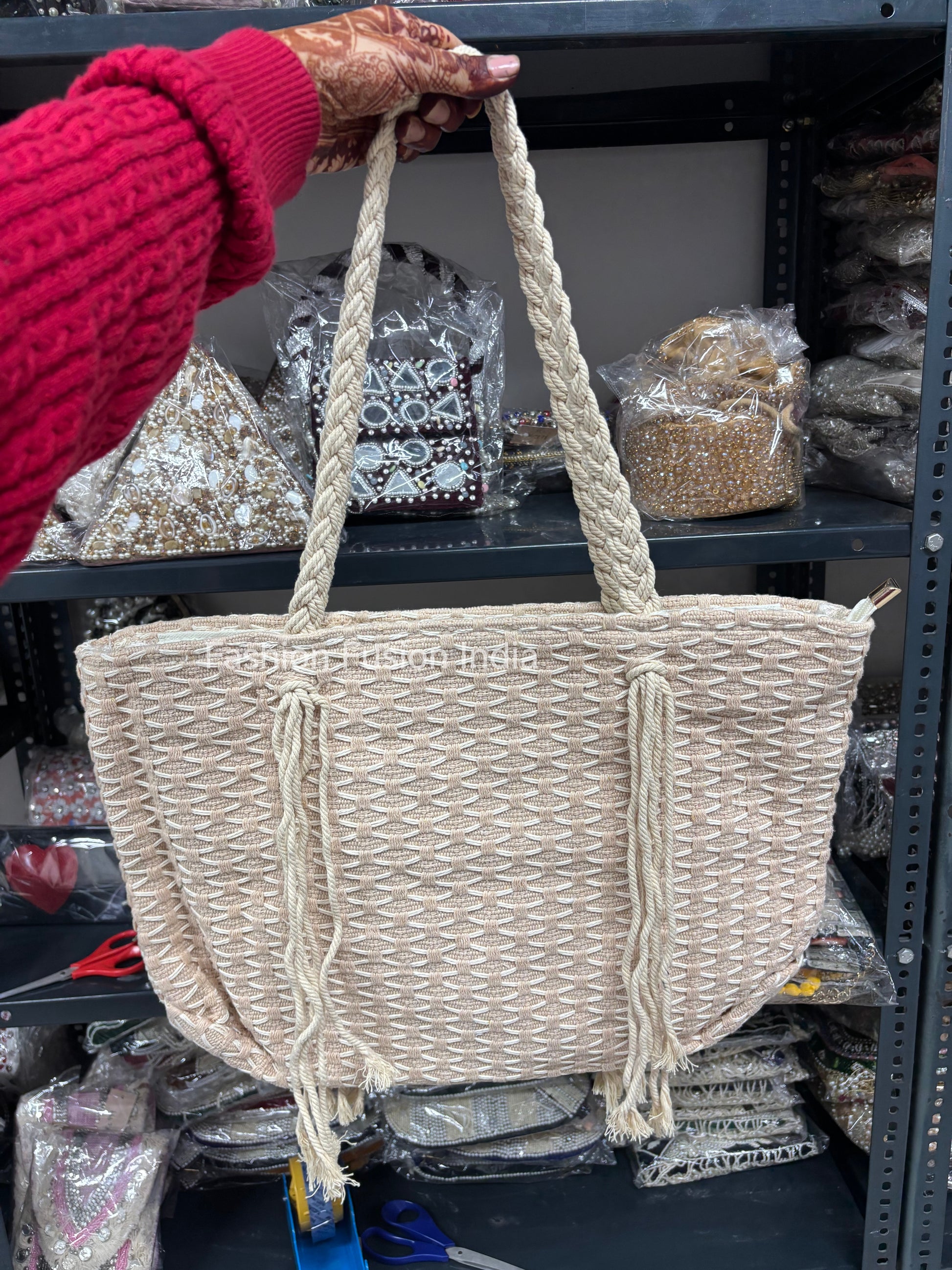 Beige woven handbag with rope handles held by a person wearing a red sweater.