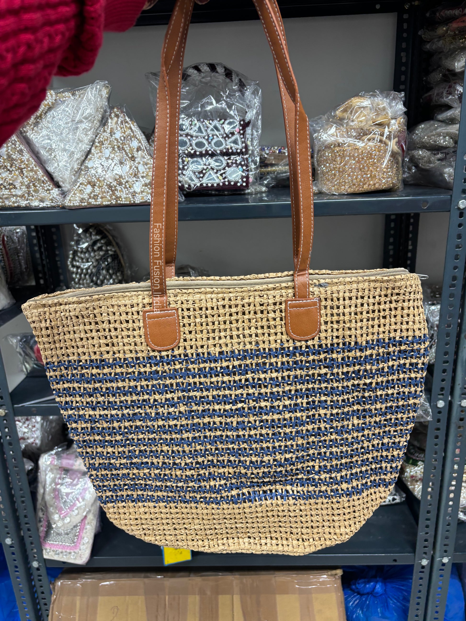 Woven handbag with brown handles on a shelf with various items