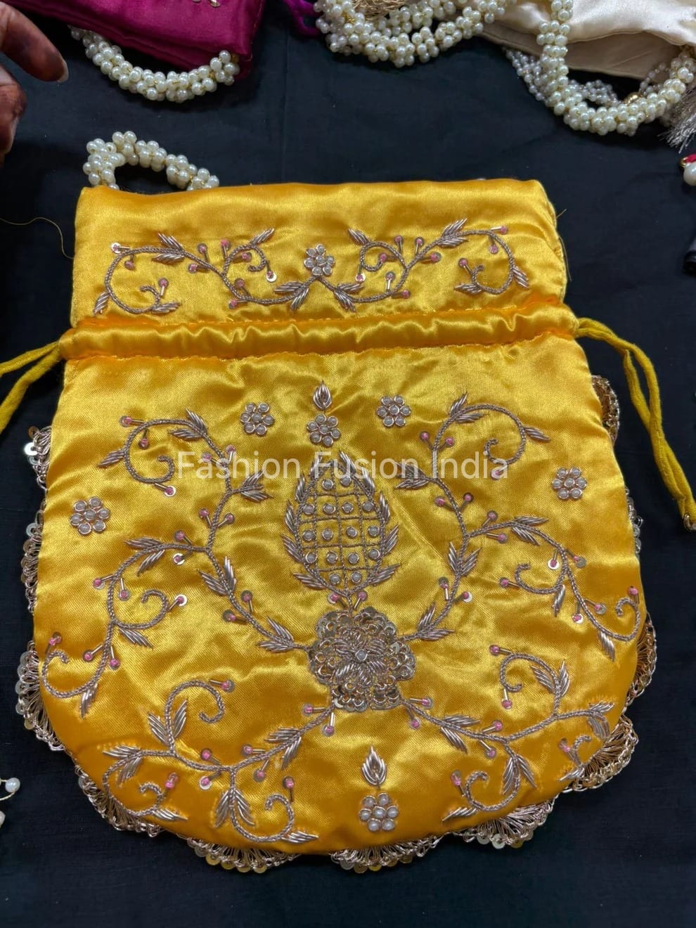 Yellow embroidered pouch with intricate designs on a dark surface, branded 'Fashion Fusion India'.