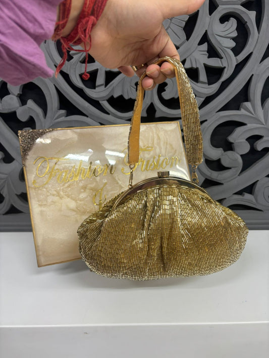 Gold beaded handbag held by a hand with a decorative background