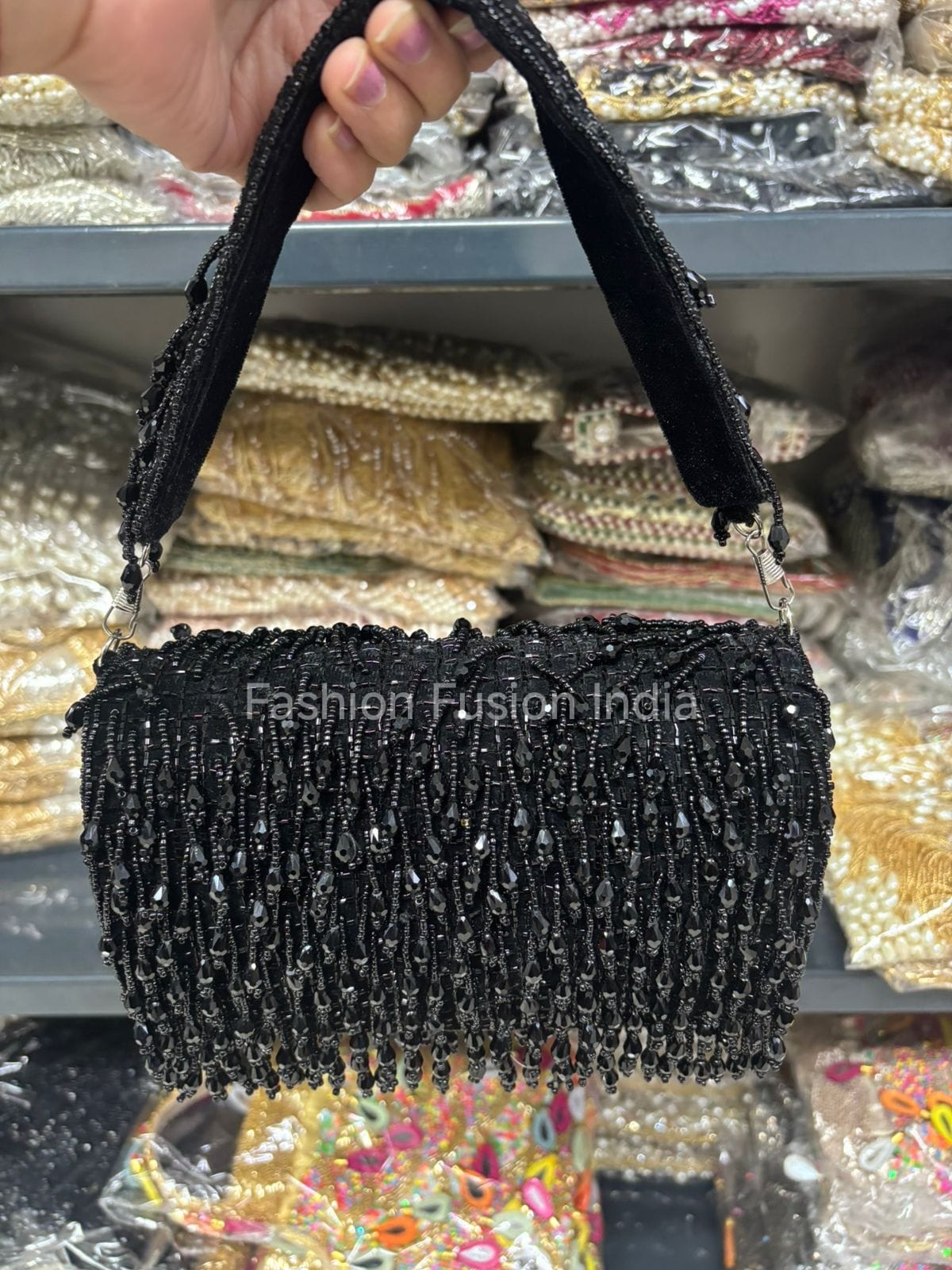 Black beaded handbag held by a hand with a blurred background of fabric samples.