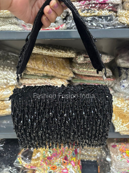 Black beaded handbag held by a hand with a blurred background of fabric samples.