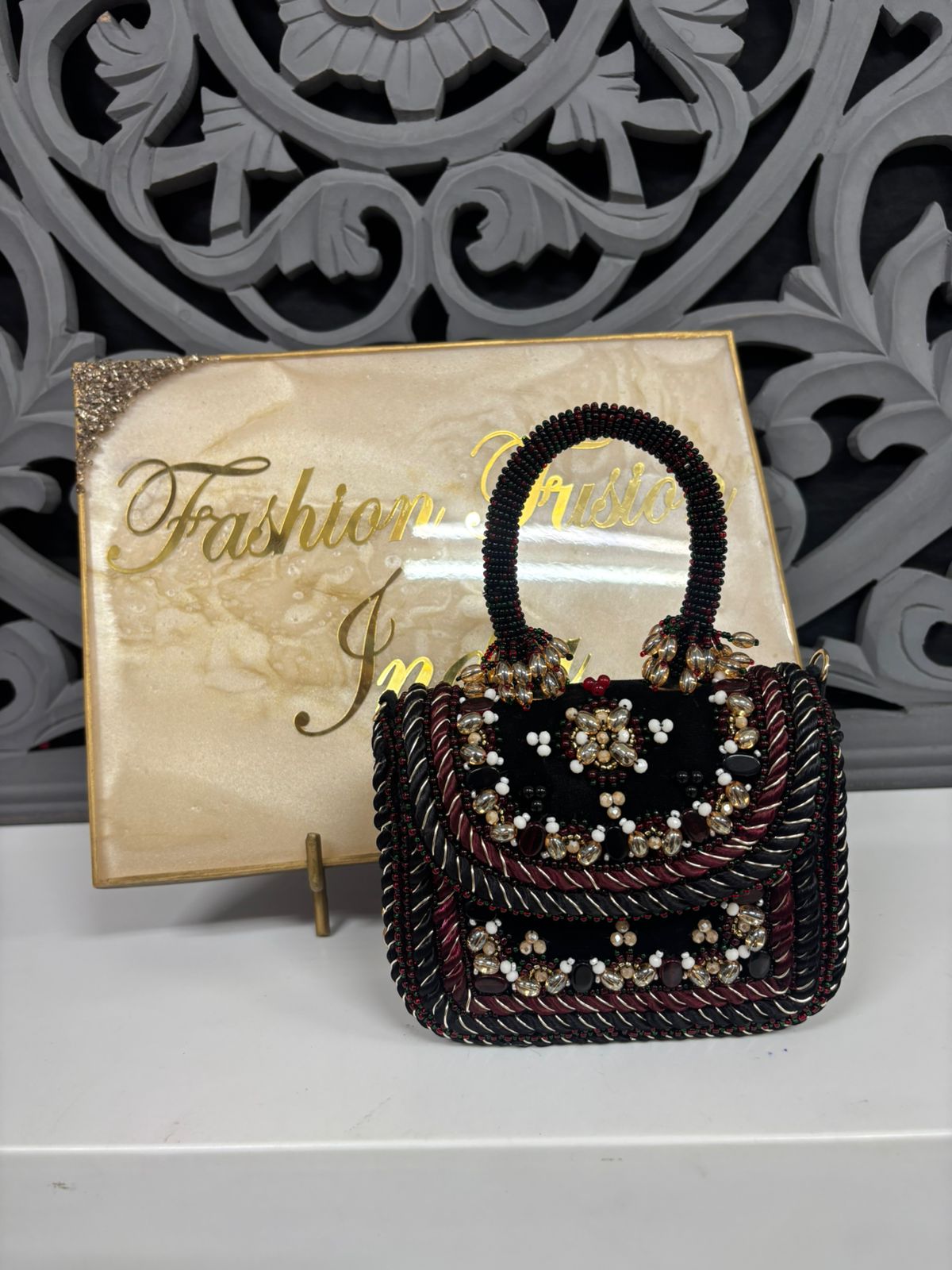 Decorative handbag with embellishments in front of a 'Fashion India' sign.