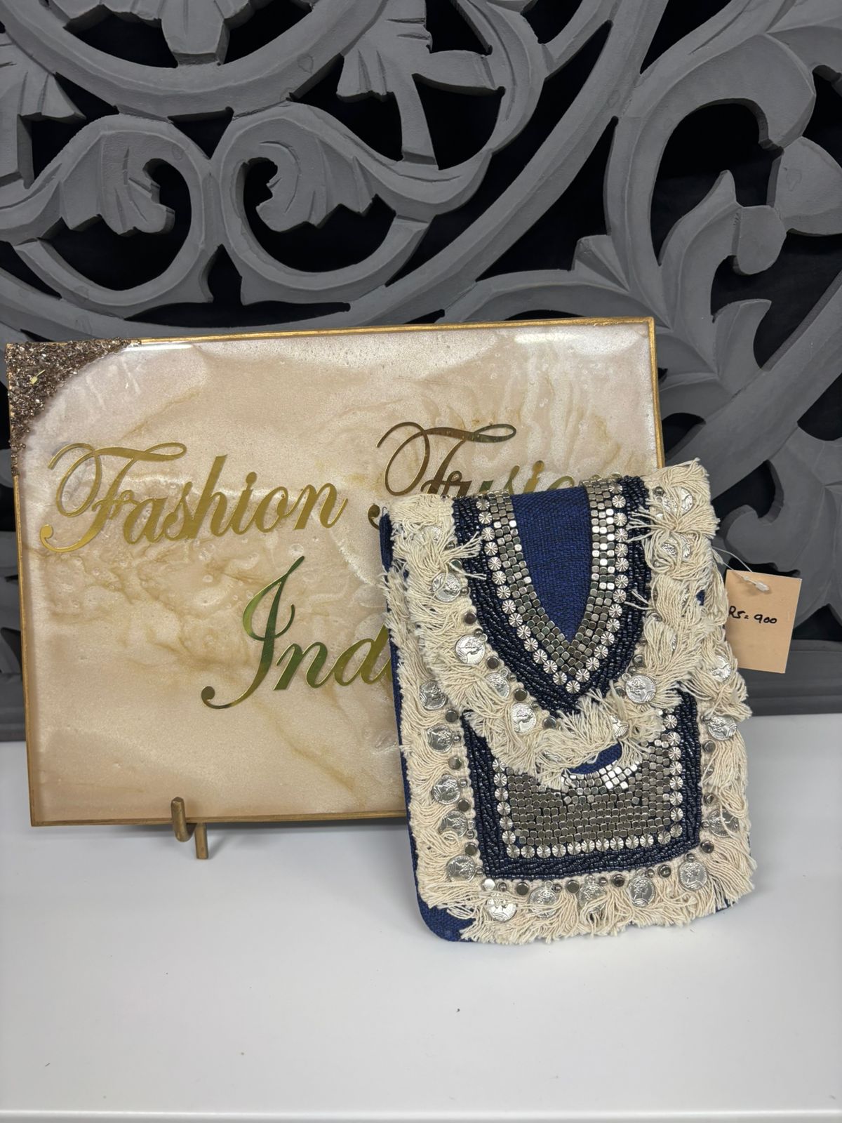 Decorative handbag with intricate design on a stand with 'Fashion India' branding.