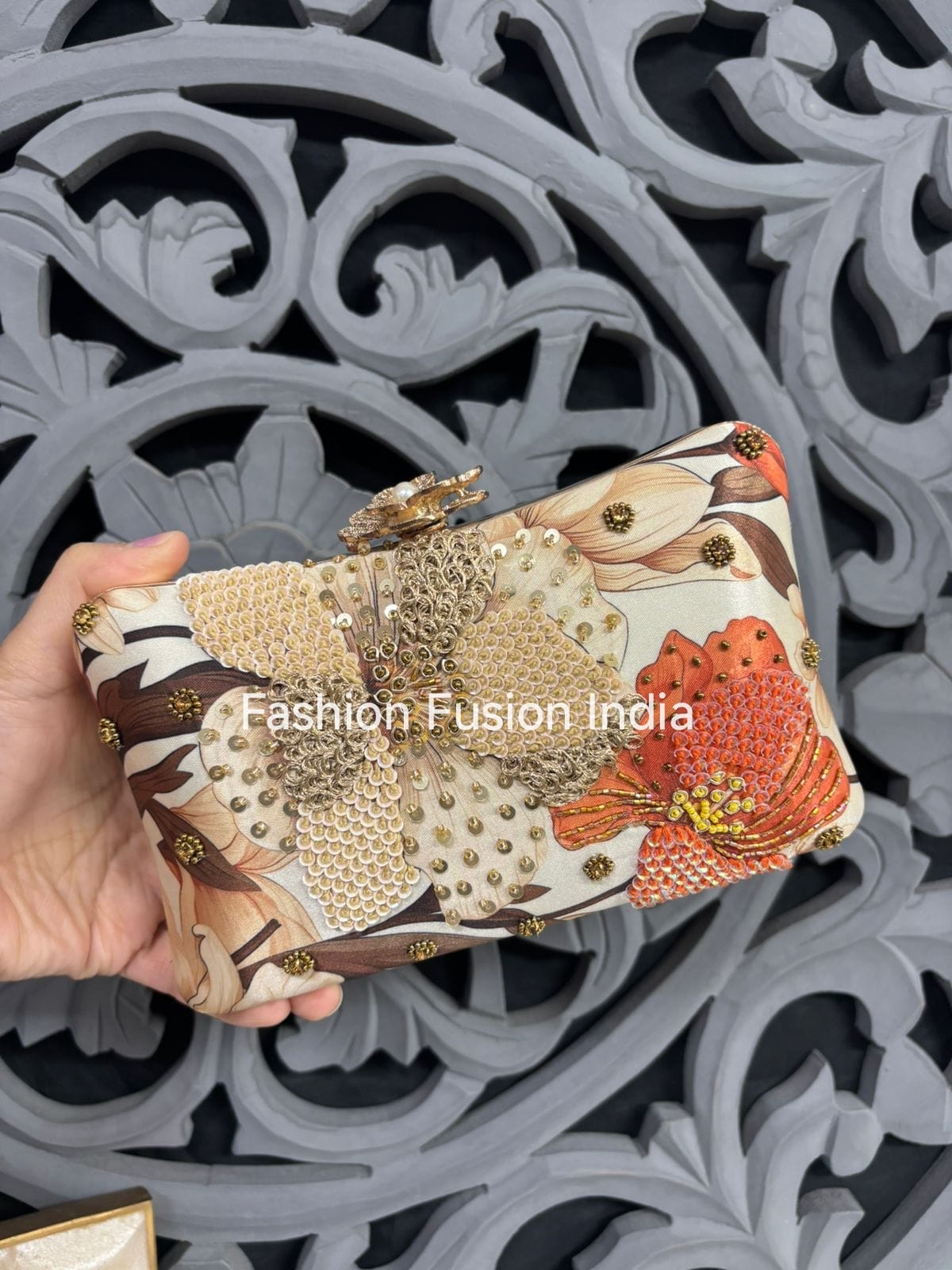 Decorative clutch held by a hand with 'Fashion Fusion India' branding against an ornate background.