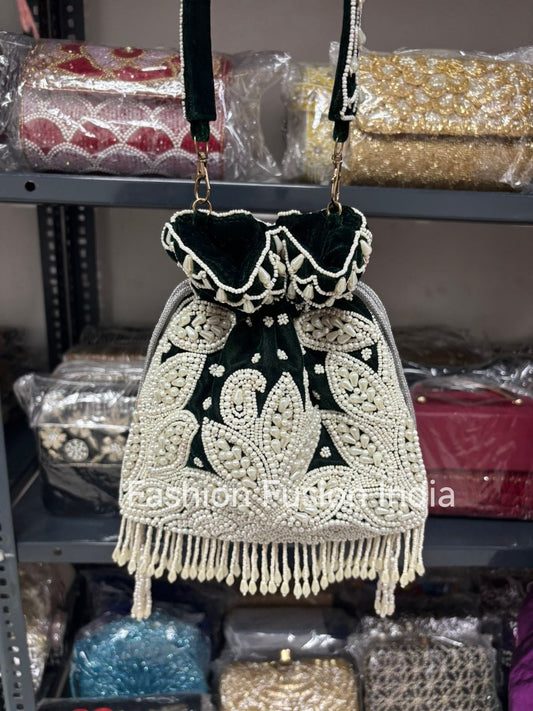 A dark green handbag with white embroidery and fringes on a shelf with other bags.