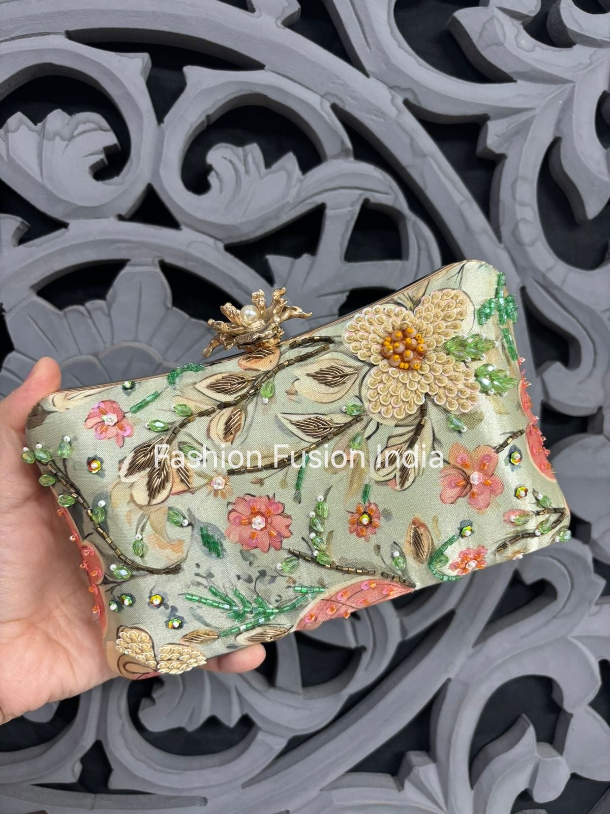 Decorative clutch with floral patterns held against an ornate gray background, branded 'Fashion Fusion India'.