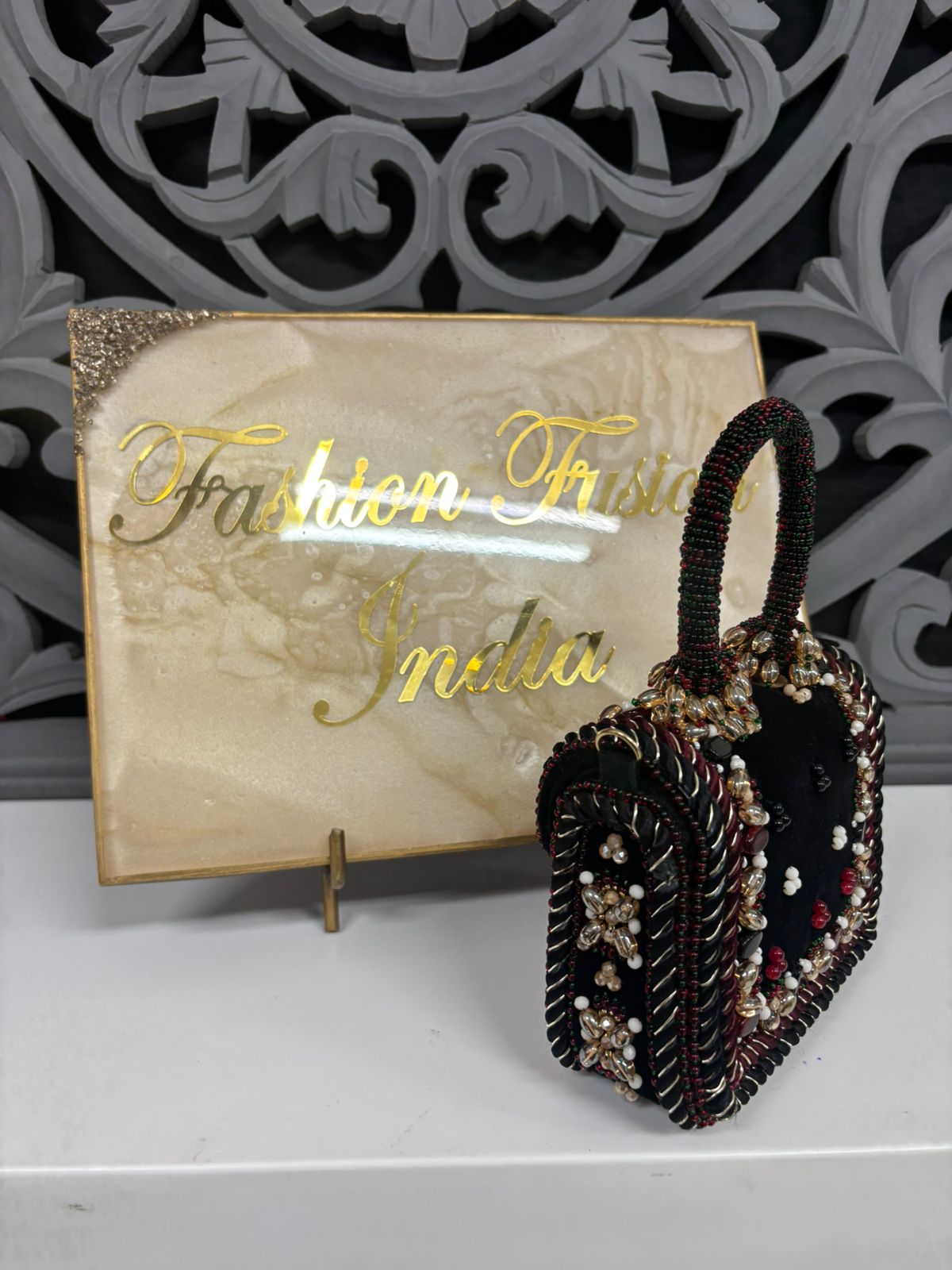 Decorative handbag with intricate beading in front of a 'Fashion Trunk India' sign.